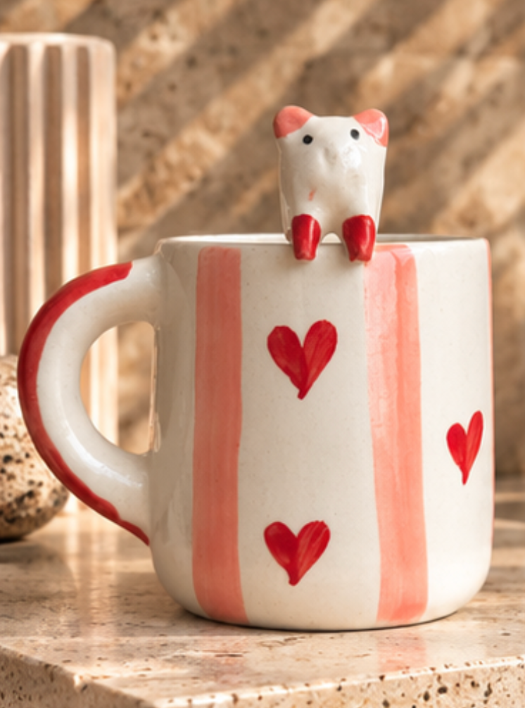 White mug with pink stripes, red hearts, and a cat perched on the rim