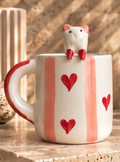 White mug with pink stripes, red hearts, and a cat perched on the rim